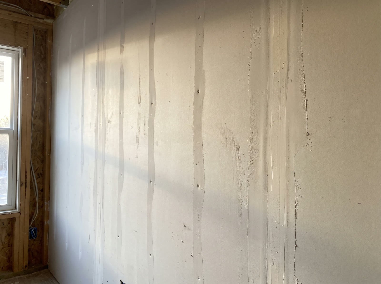 A freshly taped and mudded drywall wall in afternoon light, seams coated and screws covered, mid-finish