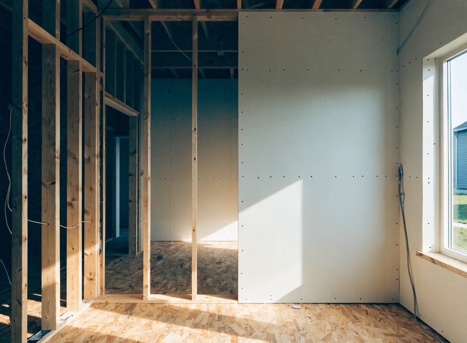 A room under construction, half bare wood framing and half newly hung drywall fastened in neat rows of screws